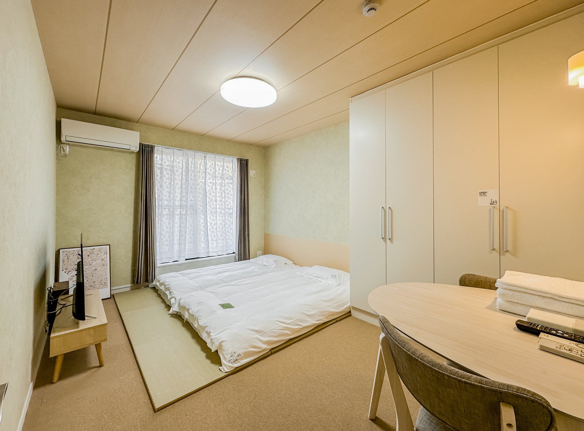A hotel room with a bed, a desk, a chair, a wardrobe, and a window with curtains.