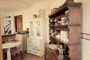 Eine Küche mit Esstisch, weißen Schränken und einem Holzregal mit Küchenutensilien.