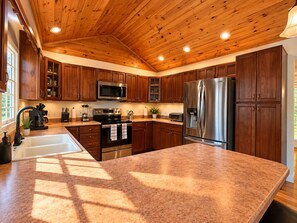 Una cocina con armarios de madera, electrodomésticos de acero inoxidable, encimera de granito y techo de madera.