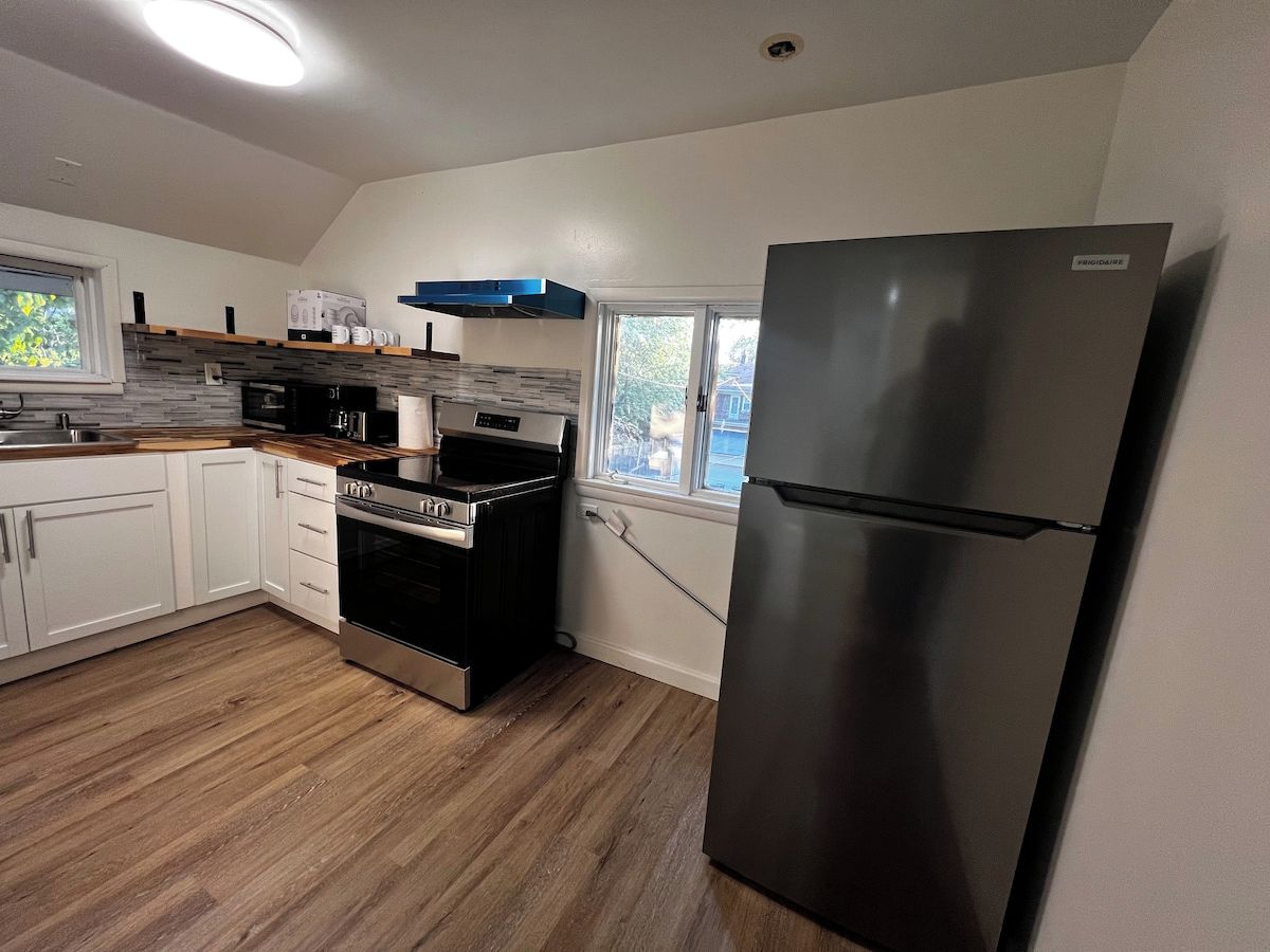 A kitchen with white cabinets, a stainless steel refrigerator, a built-in oven, and a window with a view of the outside.
