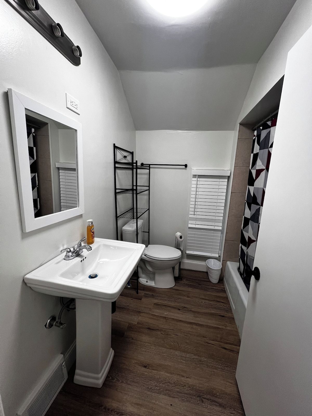 Un baño pequeño con lavamanos, inodoro y zona de ducha blancos.