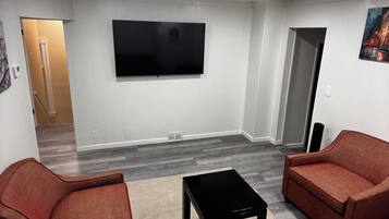 A room with a flat-screen TV mounted on the wall, two sofas, a coffee table, and a carpeted floor.