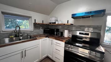 Una cocina moderna con armarios blancos, estufa de acero inoxidable y ventana que proporciona luz natural.