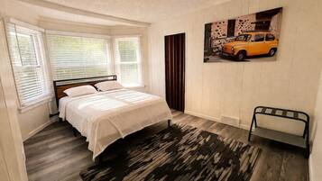 A bedroom with a bed, a window with blinds, a radiator, a rug, and a wall-mounted shelf.