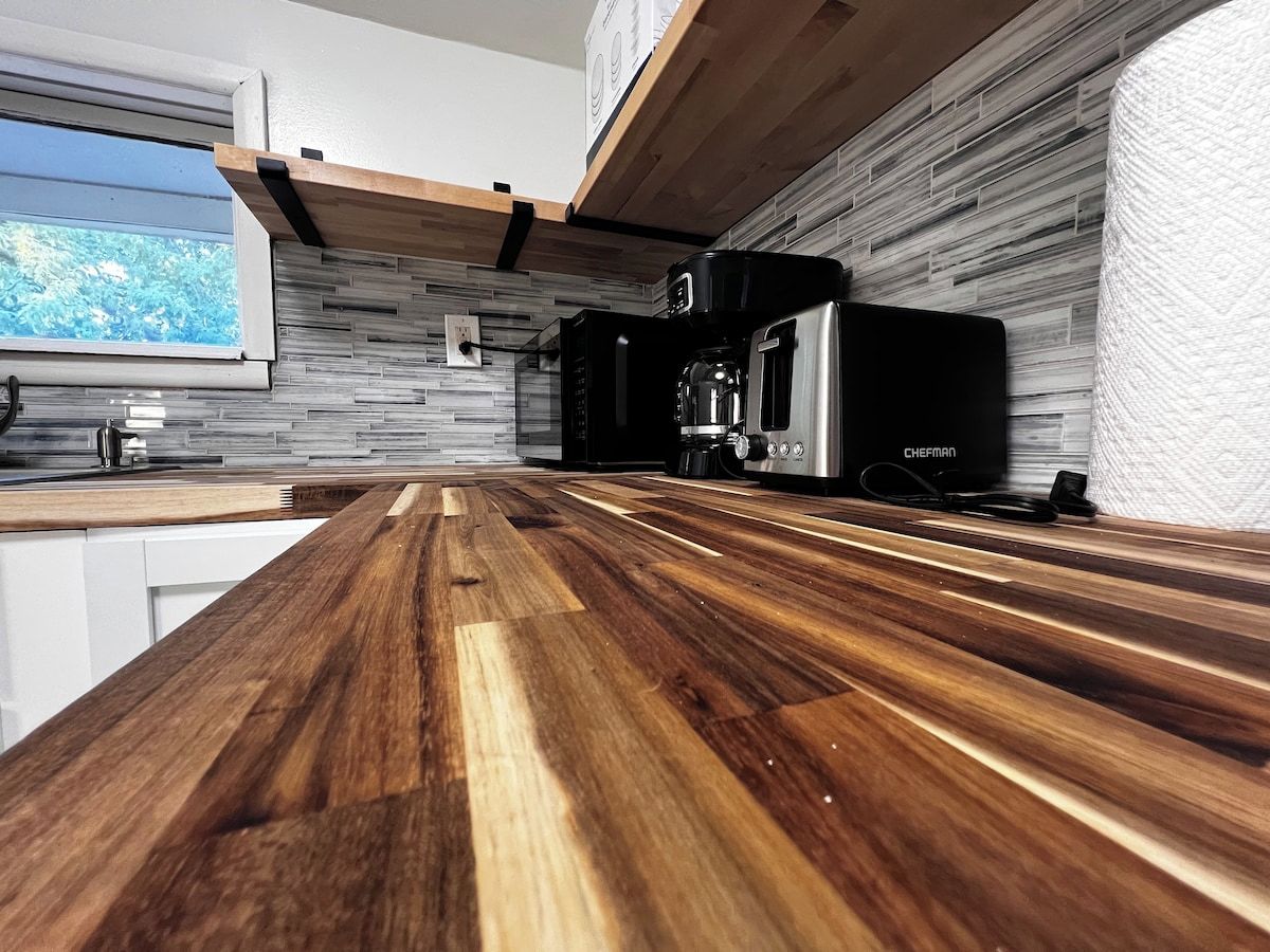 Une cuisine moderne dotée d’un plan de travail en bois, d’un four encastré et d’une fenêtre donnant sur un espace verdoyant.
