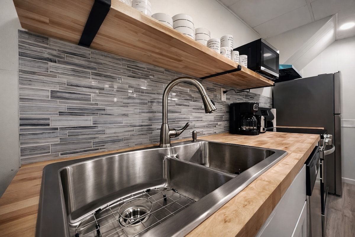 A modern kitchen with a stainless steel sink, wooden countertop, and a tiled backsplash.