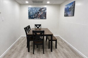 Sala de conferência com mesa retangular e quatro cadeiras, paredes brancas e duas pinturas.