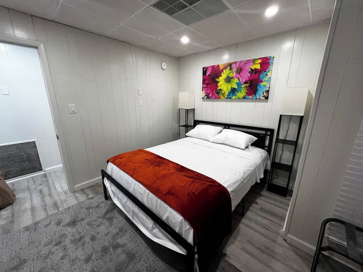 Une chambre à coucher avec un lit, une décoration murale florale aux couleurs vives, une porte blanche et un tapis gris.