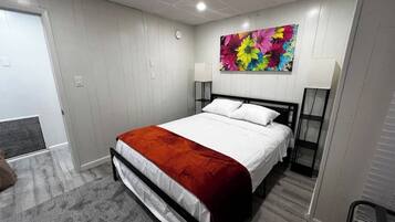 Une chambre à coucher avec un lit, une décoration murale florale aux couleurs vives, une porte blanche et un tapis gris.