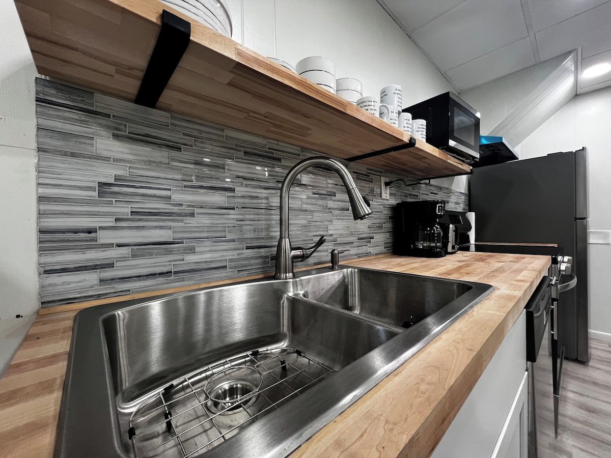 A modern kitchen with a stainless steel sink, wooden countertop, and a tiled backsplash.
