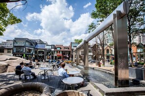Ein Sitzbereich im Freien mit Tischen und Stühlen, ein Kiesweg und ein Wasserspiel.