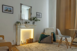 A living room with a fireplace, a chair, a table, and a mirror on the wall. - Krakow Old Town Within Easy Reach - Kazimierz Apartment (Kraków)