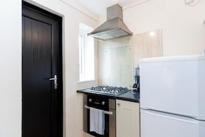 Een kleine keuken met een zwarte deur, een gasfornuis, een oven en een witte koelkast.