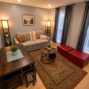 A living room with a sofa, a coffee table, a dining table, and a red bench. - Romantic getaway Skyline View for Family of 6 (Niagara Falls)