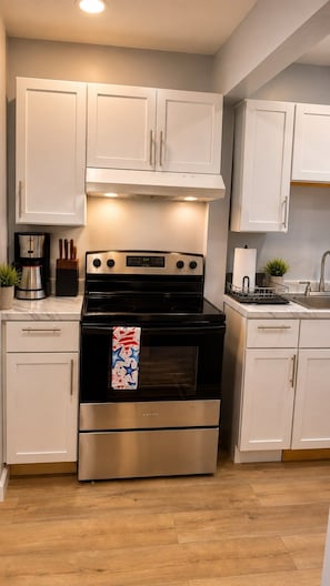 A kitchen with white cabinets, a stainless steel stove, and a coffee maker. - Romantic getaway Skyline View for Family of 6 (Niagara Falls)