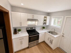 A modern kitchen with white cabinets, a stainless steel oven, a sink, and a window with blinds. - Casa Bellavista | Walk to Falls | Skyline Views (Niagara Falls)