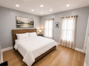 Een slaapkamer met een houten bed, een nachtkastje met een lamp en een schilderij aan de muur.