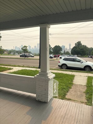 A covered outdoor area with a brick column, a paved walkway, and a view of a city skyline with buildings and a tower. - Whole 621 Home - Sleeps 16 - Walk to Falls (Niagara Falls)