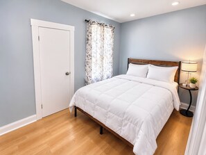 A bedroom with a bed, a door, a curtain, and a bedside table with a lamp. - Whole 621 Home - Sleeps 16 - Walk to Falls (Niagara Falls)