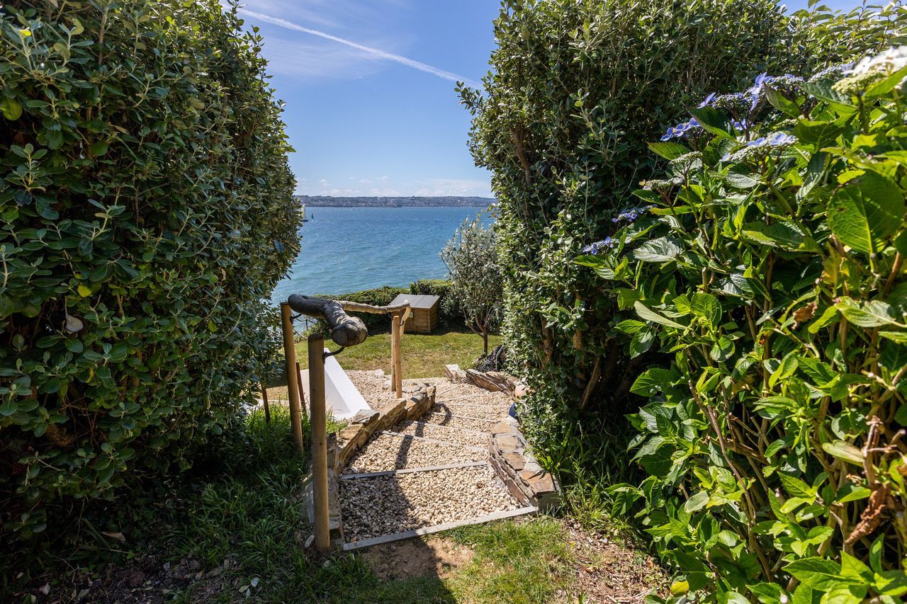 A garden pathway leading to a body of water, surrounded by dense foliage.