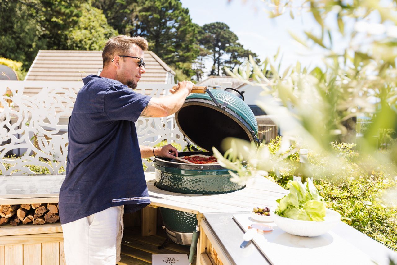 A person cooking outdoors with a large green pot on a table.