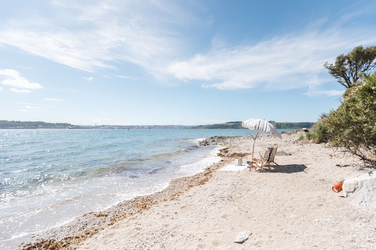 Ein Strand mit blauem Himmel, ruhiger See und einem einzelnen Sonnenschirm, der Schatten spendet.