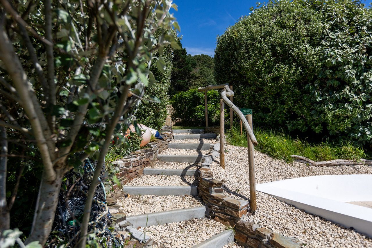A garden pathway with stone steps leading to a white platform, surrounded by greenery and trees.