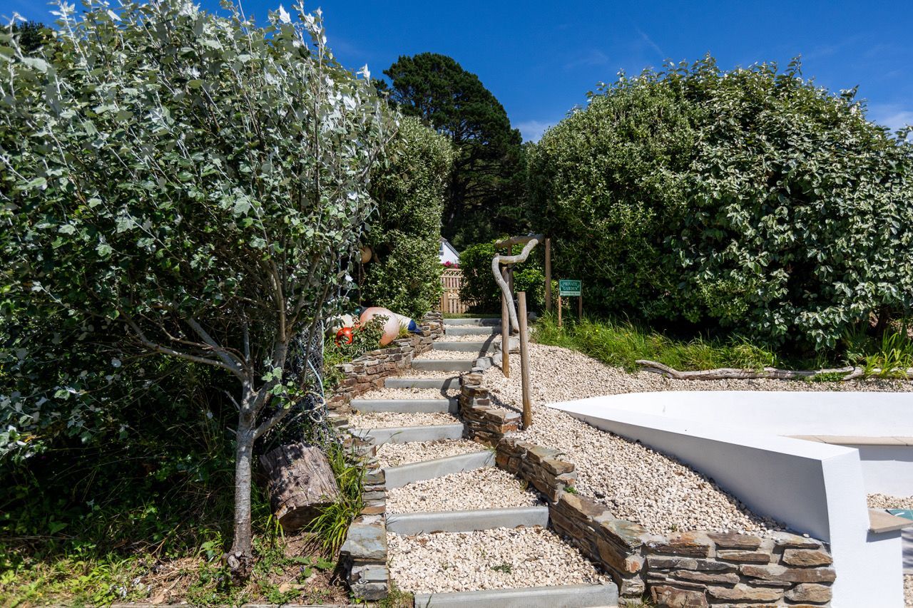 A pathway leading through a garden with stone steps and a white wall on one side.