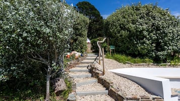 A pathway leading through a garden with stone steps and a white wall on one side.