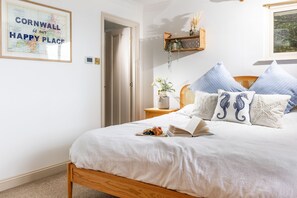 Ein Schlafzimmer mit einem Bett, Kissen, einem Nachttisch mit einem Buch und einer Vase, einer gerahmten Karte an der Wand und einer Tür.