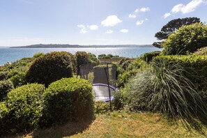Ein Garten mit Trampolin, einem Weg und Blick auf das Meer.