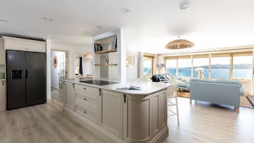 A modern kitchen with a central island, a dining area with a view, and a living room with a sofa and a large window.