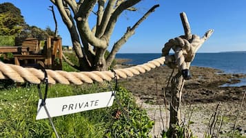 A rope barrier with a 'PRIVATE' sign, a wooden bench, and a tree by a beach.