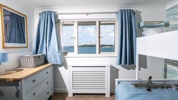 A bedroom with a view of the sea, a bunk bed, a desk with a lamp, and a dresser.