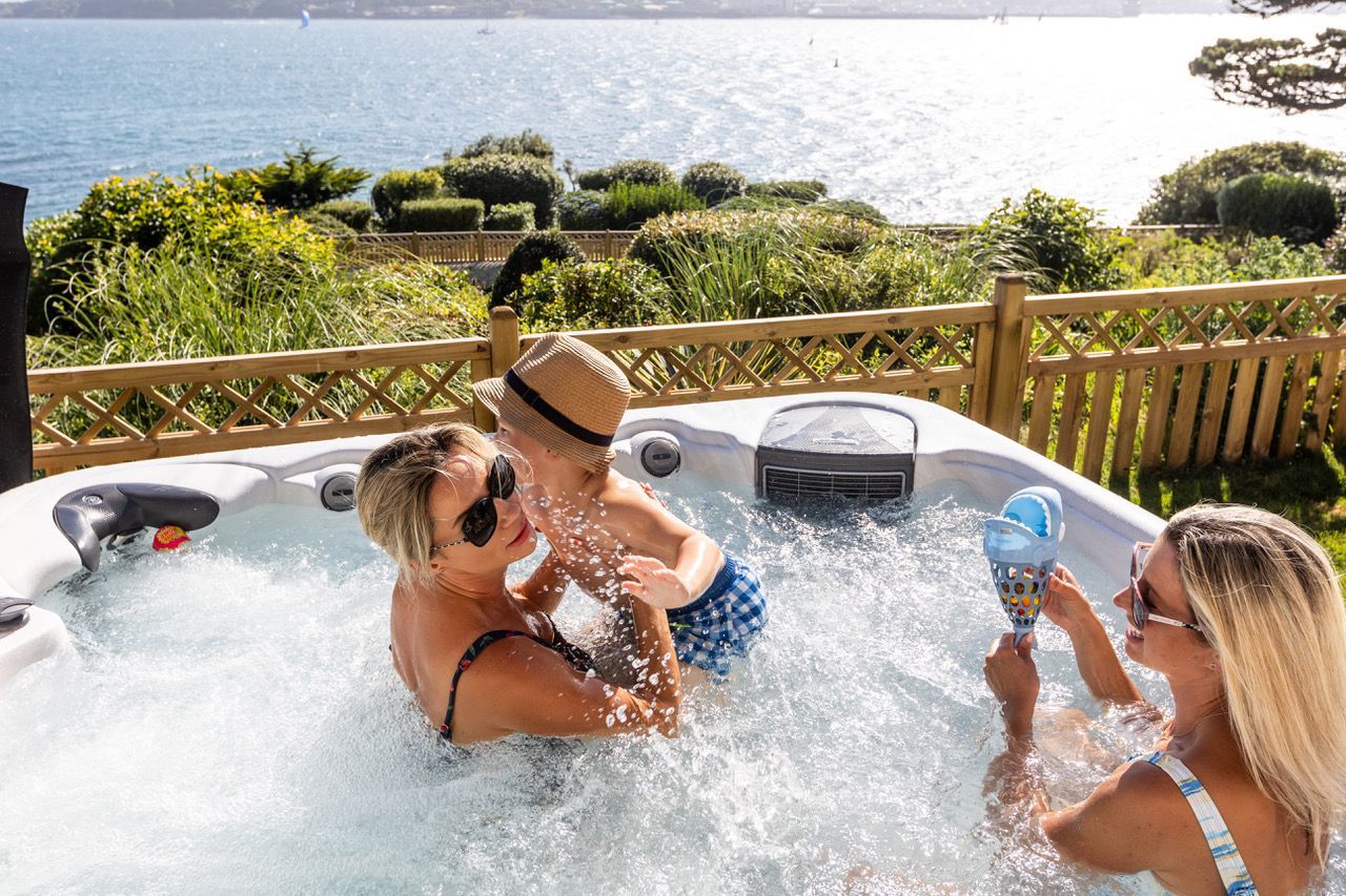 Ein Whirlpool mit zwei Personen, umgeben von einer Holzterrasse und viel Grün.