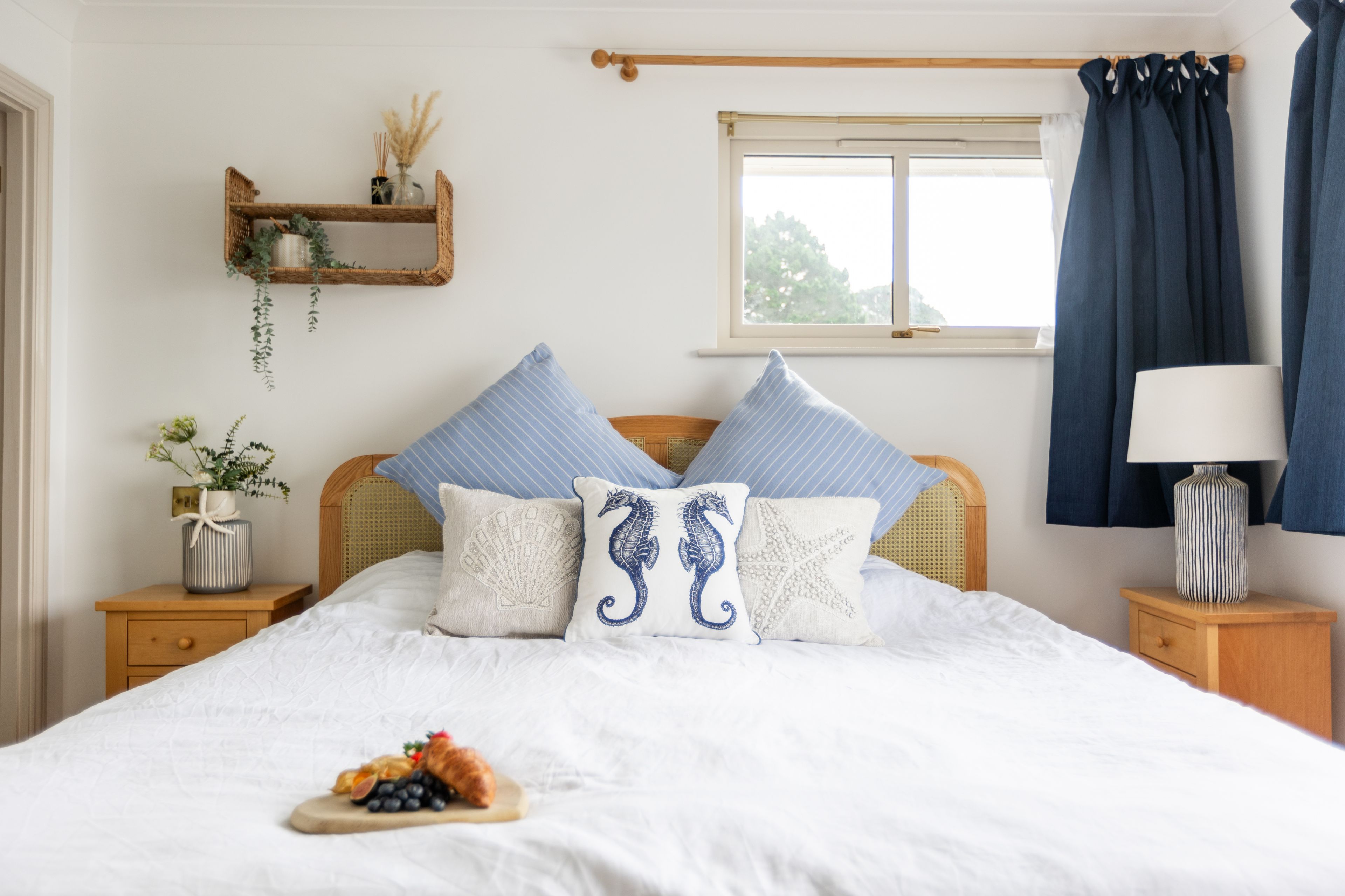 Ein Schlafzimmer mit einem Bett, Kissen, einem Nachttisch, einem Fenster mit Vorhängen und einem Wandregal mit Dekoration.