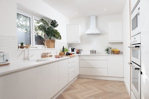 A modern kitchen with white cabinetry, a large window, and a herringbone wood floor. - Meadow Retreat - Sleeps 12 | 4 Bedrooms | Hot Tub | Sauna | Cinema Room | Games Room | Dog Friendly (Hatt, Saltash, Cornwall)