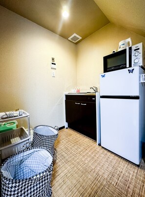 A compact kitchenette with a refrigerator, microwave, and sink. There are two baskets and a small table with items on it. - HANASTAY EBIYA HIGASHI (Osaka)
