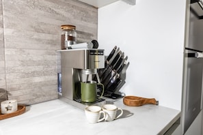 Una cocina con una cafetera, un bloque de cuchillos y dos tazas sobre la encimera.