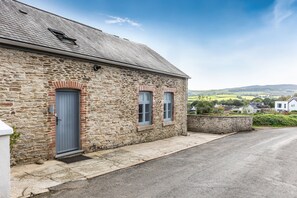 A stone building with a grey door and windows, a paved driveway, and a view of a rural landscape. - The Valley Hideaway  - sleeps 2 guests  in 1 bedroom (Harrowbarrow, Callington)