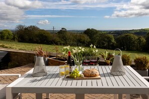An outdoor dining table with a view of the countryside, a bottle of wine, glasses, and a loaf of bread. - The Valley Hideaway  - sleeps 2 guests  in 1 bedroom (Harrowbarrow, Callington)