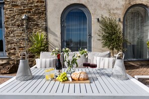 An outdoor dining area with a table set for two, featuring a bottle of wine, a loaf of bread, a bowl of grapes, and two glasses of red wine. - The Valley Hideaway  - sleeps 2 guests  in 1 bedroom (Harrowbarrow, Callington)