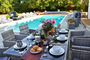 Ein Essbereich im Freien mit Pool, Korbmöbeln und einem Tisch, der für eine Mahlzeit gedeckt ist.