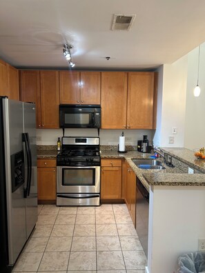 A kitchen with wooden cabinets, stainless steel appliances, a granite countertop, and a tiled floor. - Cozy 1-bedroom condo in Downtown Atlanta with fitness room and pool (Atlanta)