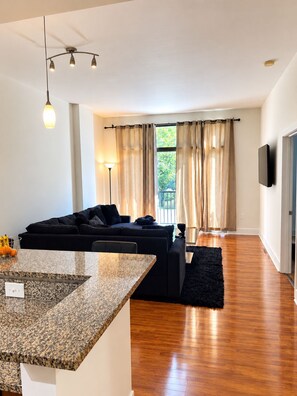 A modern living room with a black sofa, a wooden dining table, and a kitchen area with a granite countertop. - Cozy 1-bedroom condo in Downtown Atlanta with fitness room and pool (Atlanta)