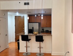 A modern kitchen with two bar stools, a refrigerator, and a countertop with a bowl. - Cozy 1-bedroom condo in Downtown Atlanta with fitness room and pool (Atlanta)