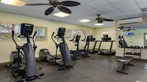 Ein Fitnessraum mit Laufbändern, Crosstrainern und einer Bank.