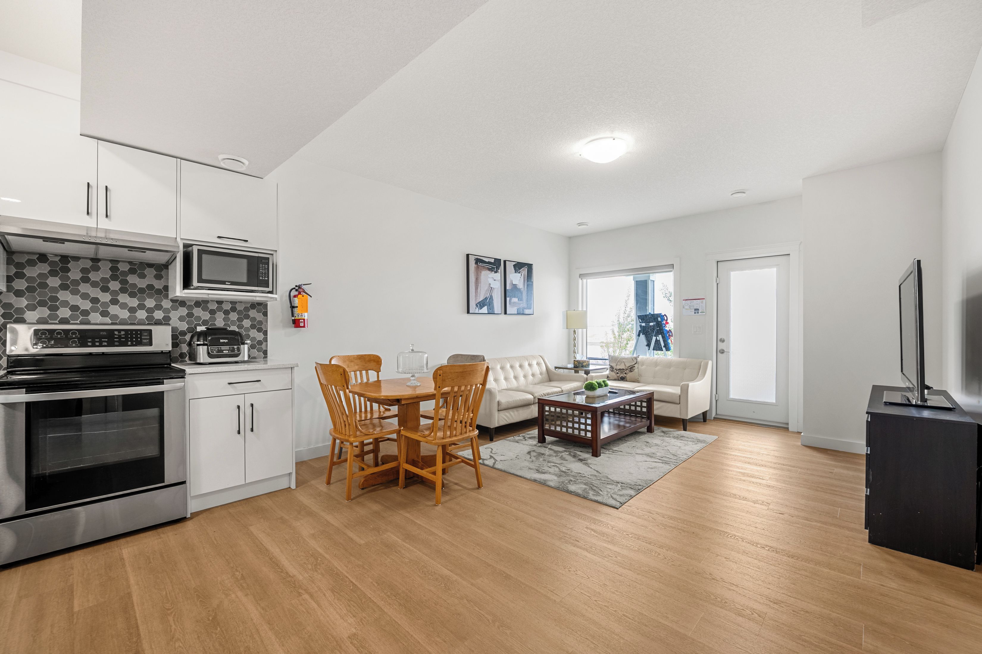 A modern kitchen with built-in appliances, a dining area with wooden chairs, a sofa, and a coffee table.
