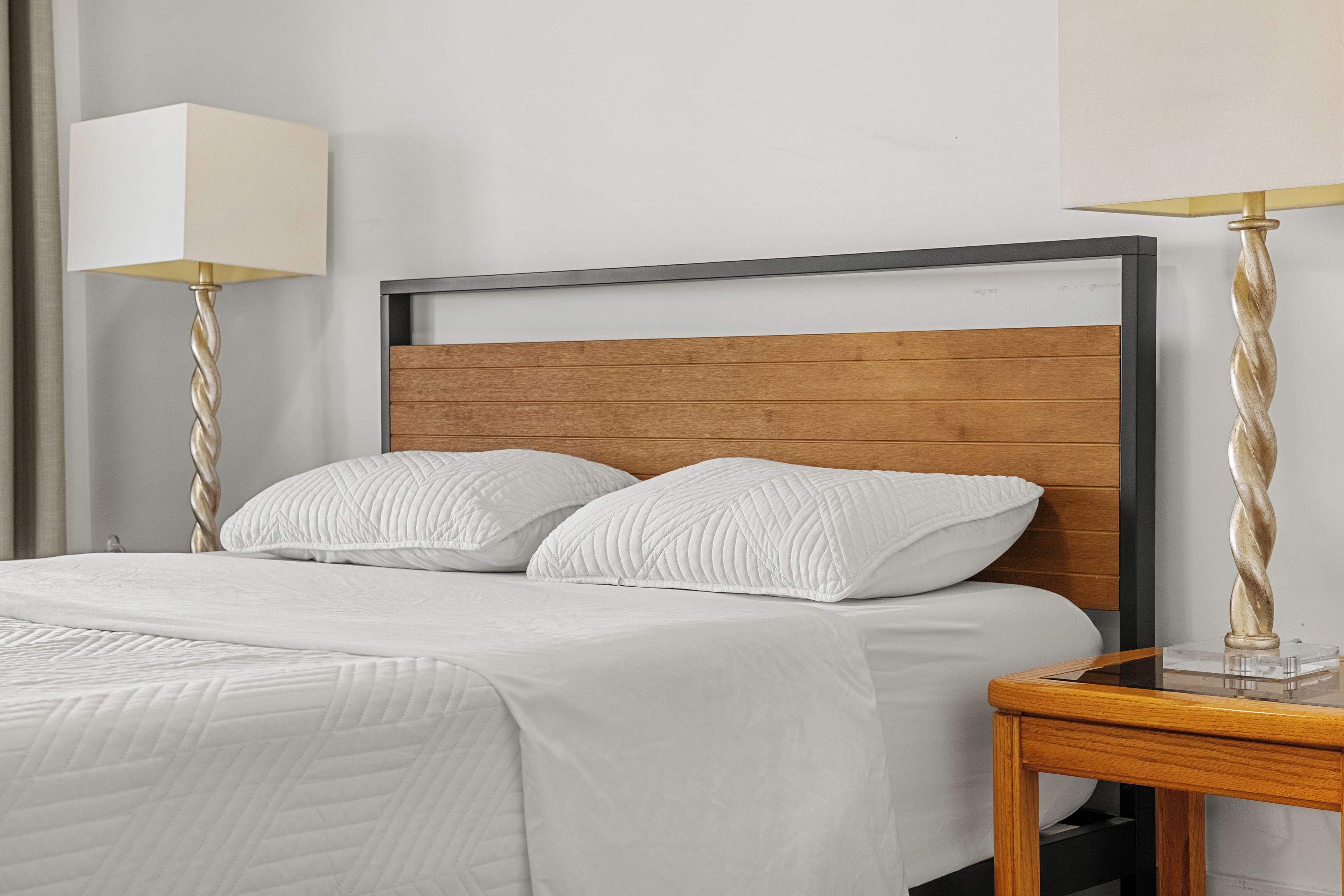 A neatly made bed with white bedding and two pillows, a wooden headboard, and two bedside tables with lamps.
