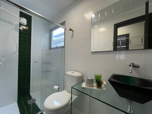 Et moderne badeværelse med en glasbrusekabine, toilet, vask og spejl.